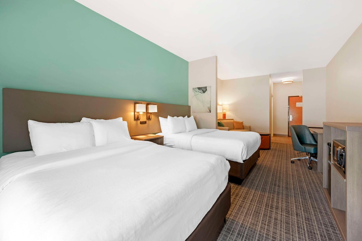 A hotel room with two beds, a desk, a chair, and a small kitchenette.