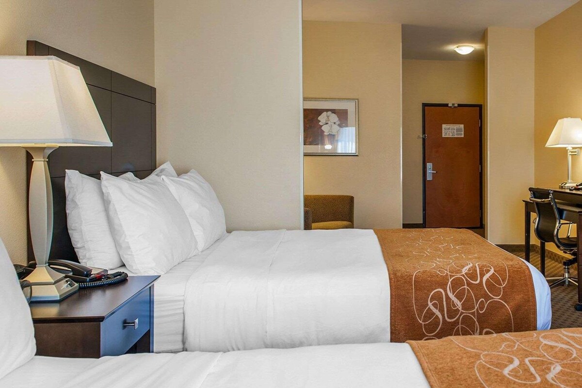 A hotel room with a bed, a desk with a lamp, a chair, and a door.
