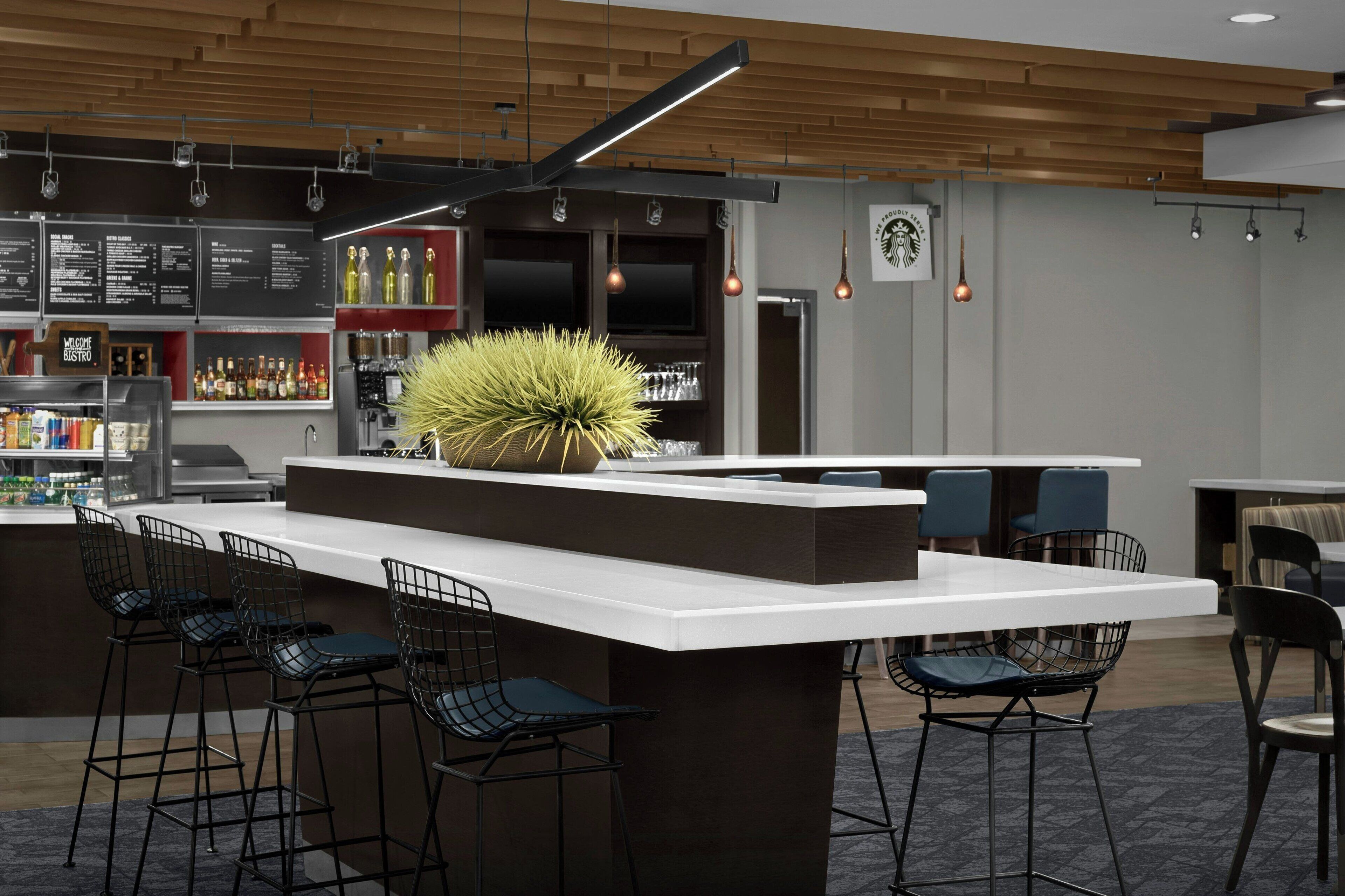 Zona de bar moderna con una barra blanca, taburetes negros y una decoración vegetal central.