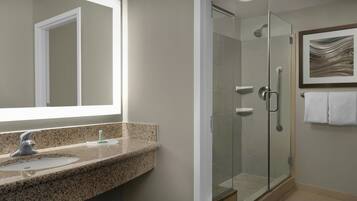 A modern bathroom with a granite countertop sink, a glass shower enclosure, and a framed abstract artwork on the wall.