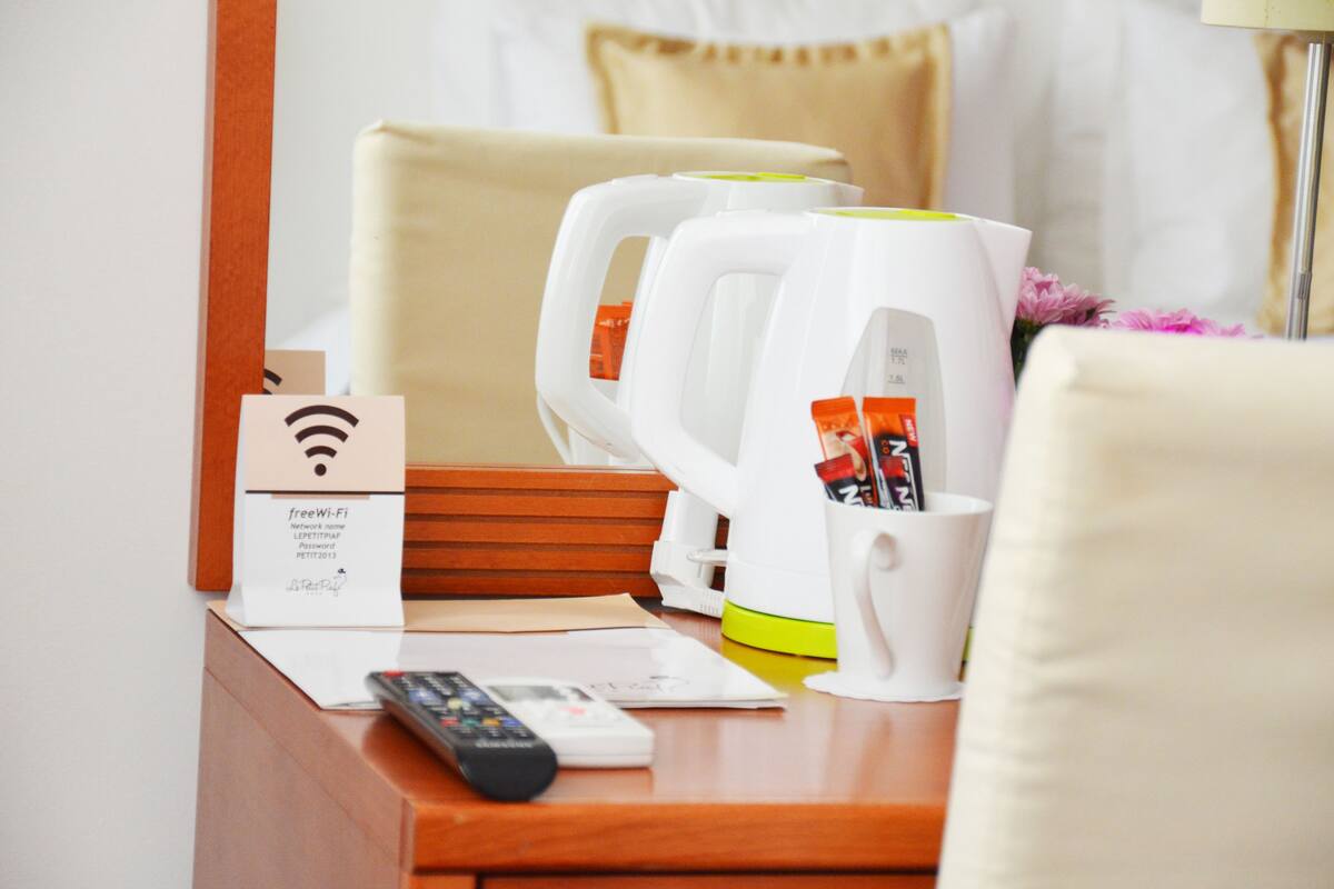 Quarto de hotel com escrivaninha de madeira, cafeteira branca, controle remoto e sinal de Wi-Fi.