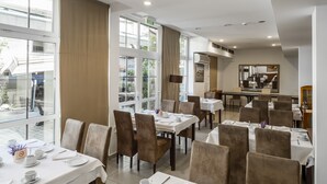 Ein Hotel-Speisesaal mit gedeckten Tischen für das Frühstück, großen Fenstern und einem Notausgang.