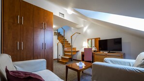Ein Hotelzimmer mit Dachschräge, einem Holzschrank, einem Schreibtisch mit Lampe, einem Fernseher und zwei Sofas.