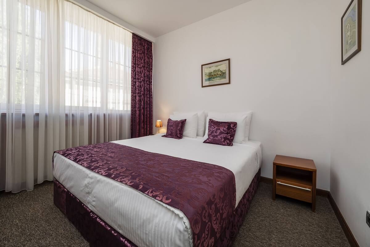 Quarto de hotel com uma cama grande, mesa de cabeceira, luminária e um quadro na parede.