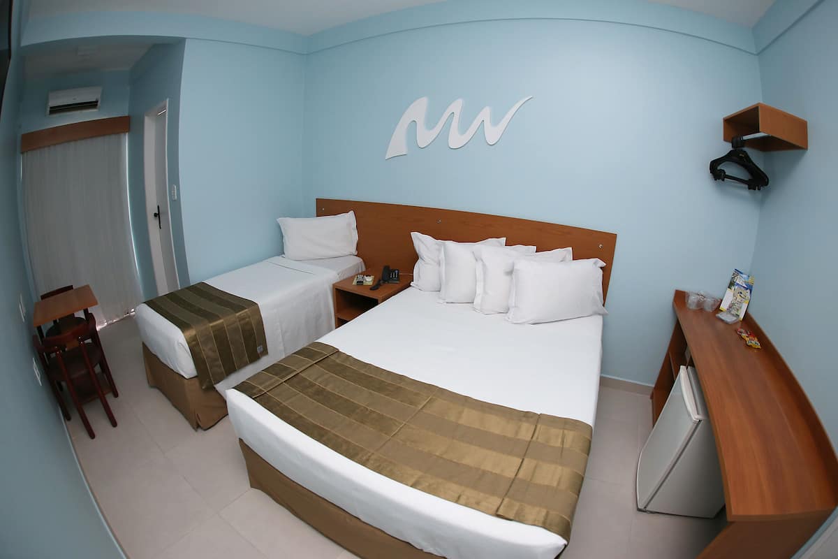 A hotel room with two beds, a desk, a chair, a wardrobe, and a small refrigerator.