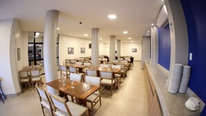 A spacious dining area with multiple tables and chairs, large pillars, and a counter with stacked plates. - Real Praia Hotel (Aracaju)