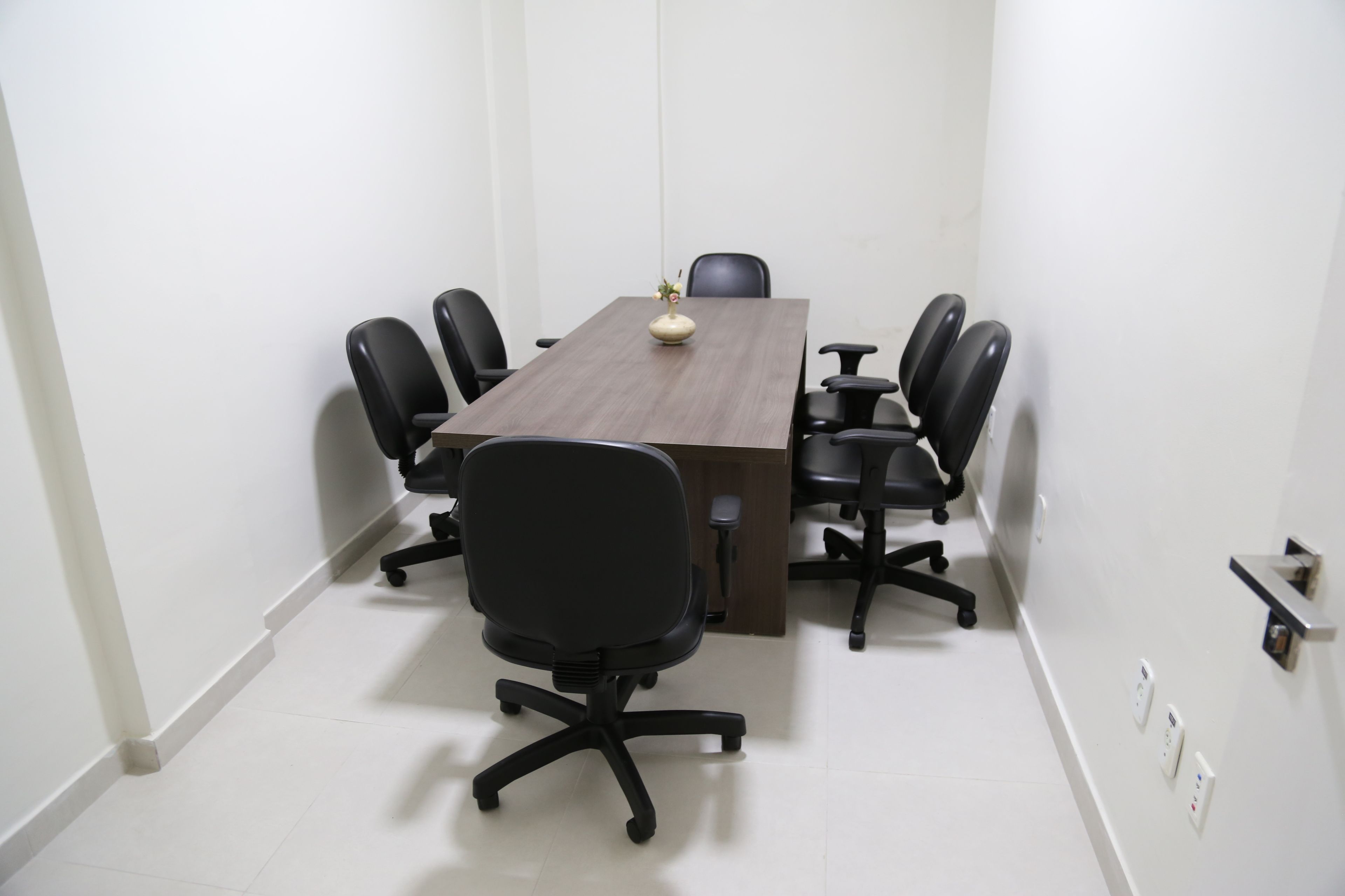 A conference room with a rectangular table, black office chairs, and a vase on the table.