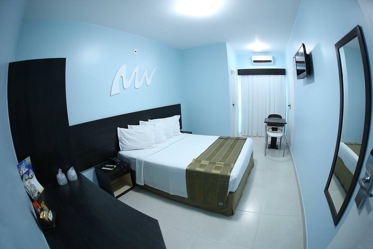 A hotel room with a bed, bedside table, chair, and a TV mounted on the wall.