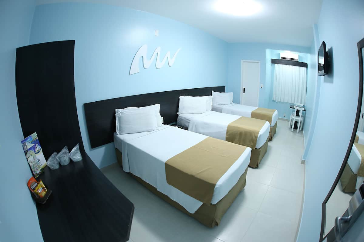 A hotel room with three beds, a desk, and a TV.