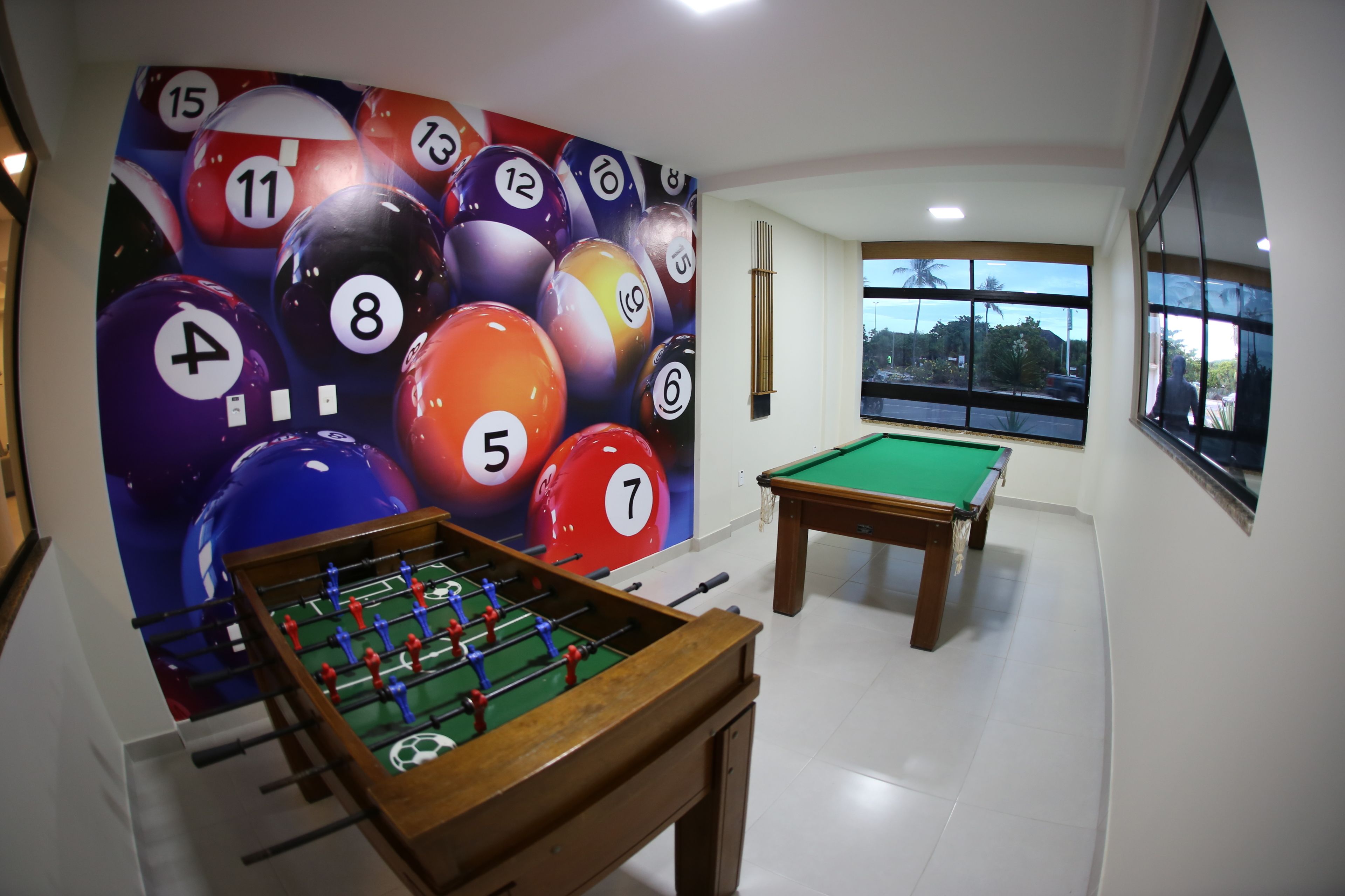 Een kamer met een tafelvoetbaltafel, een pooltafel en een muurschildering van biljartballen.