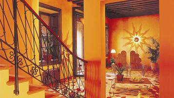 Una escalera con barandillas de metal decoradas conduce a una habitación soleada con suelo de baldosas y un gran mural de sol.