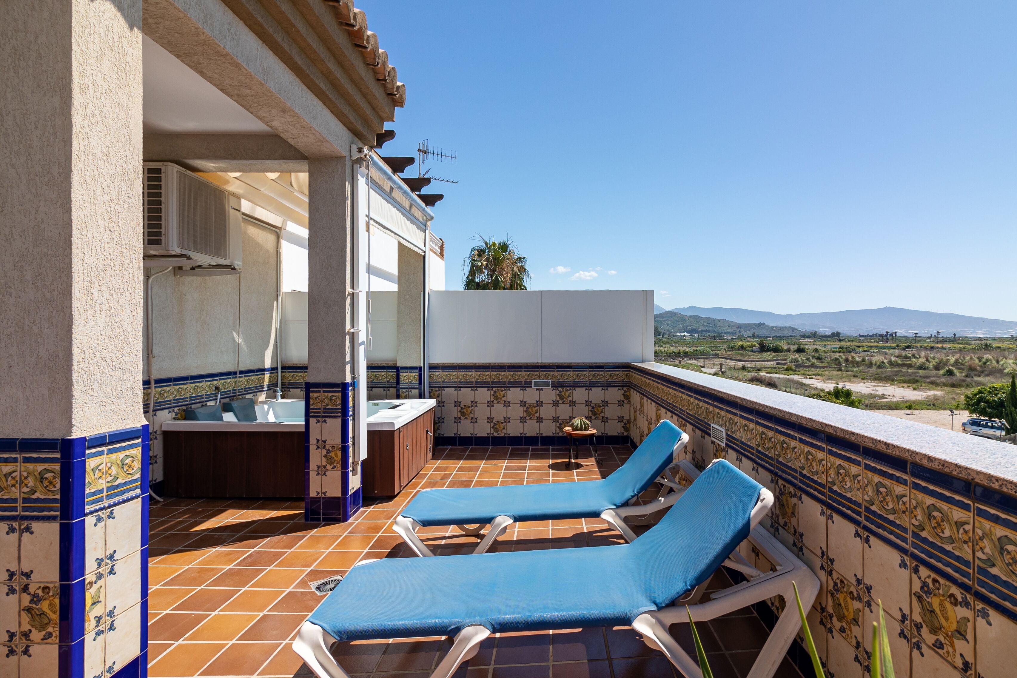 Una terraza en la azotea con dos sillones azules, una pequeña mesa y una pared decorada con azulejos.