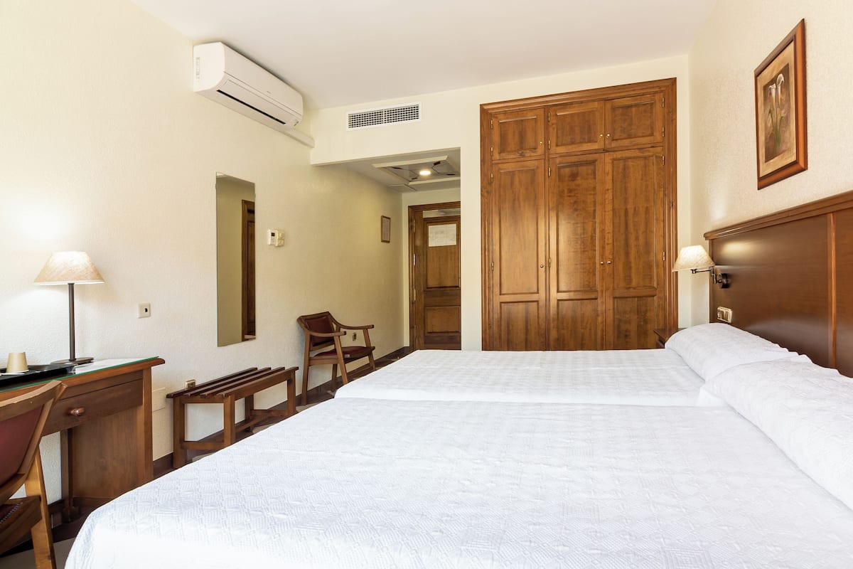 A hotel room with a large bed, a desk, a chair, and wooden wardrobes.