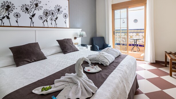 A hotel room with a bed, a chair, a table, and a balcony with a view. - Hotel Avenida Tropical (Salobreña)