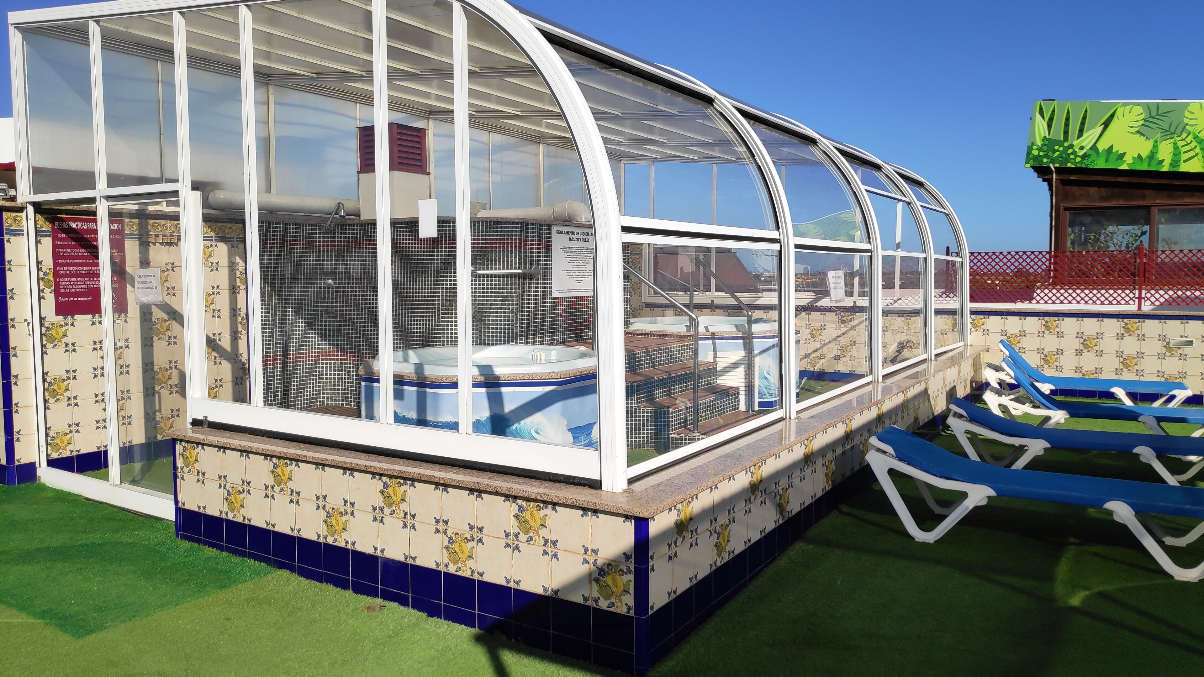 Un espacio al aire libre cubierto con un jacuzzi, sillones de descanso y una pared de azulejos con motivos florales.