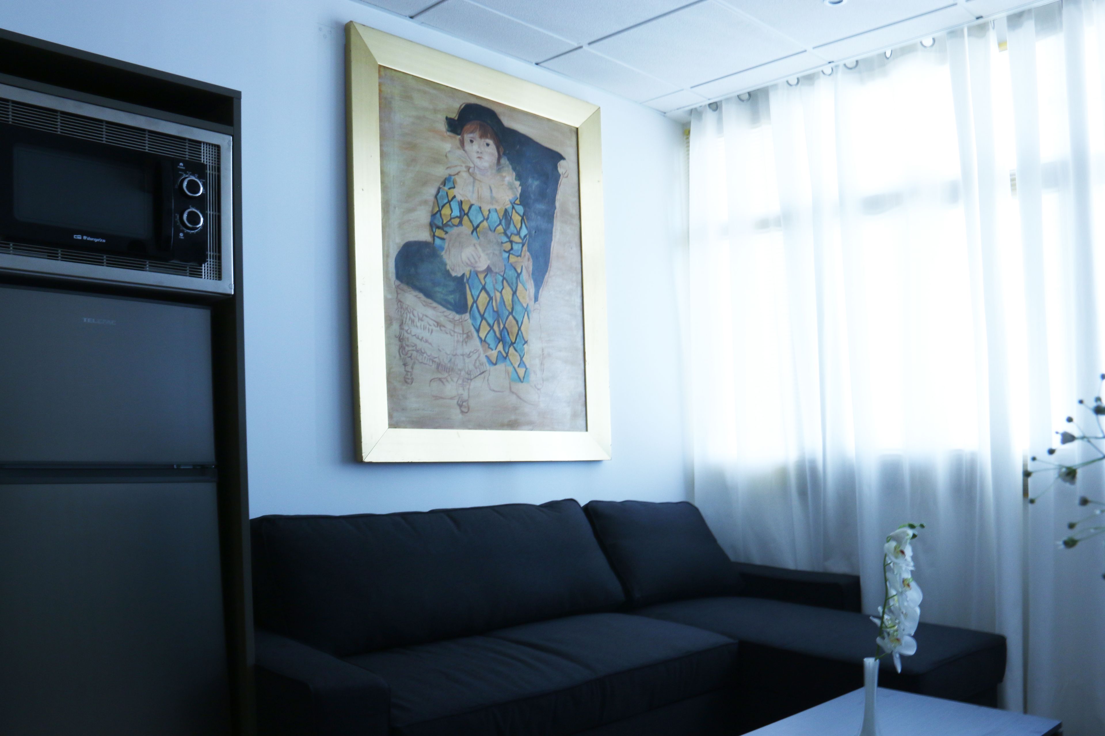 A living room with a black sofa, a framed painting, a microwave, and a vase with flowers.