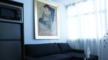 A living room with a black sofa, a framed painting, a microwave, and a vase with flowers.