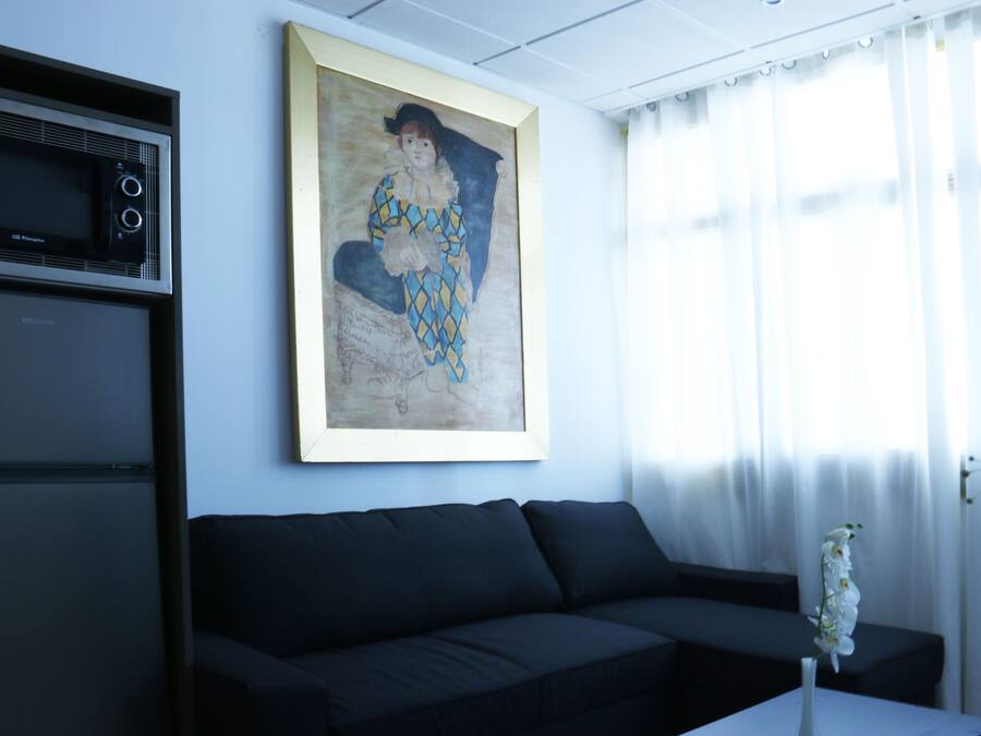 A living room with a black sofa, a framed painting, a microwave, and a vase with flowers.