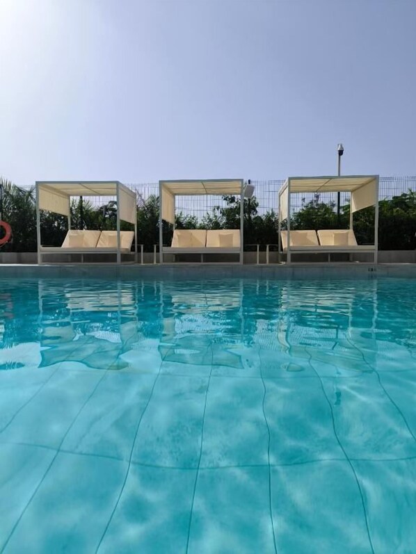 A swimming pool with clear water, surrounded by four shaded lounge areas.