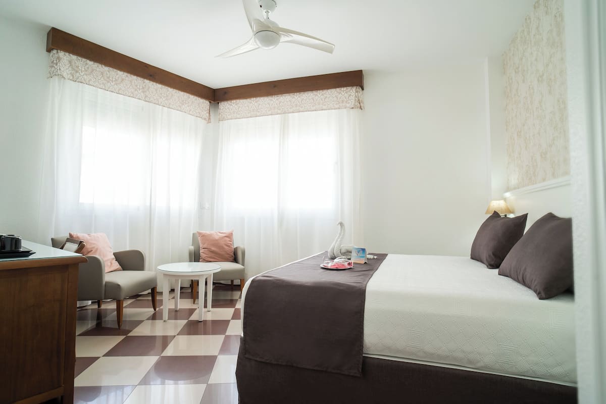 A hotel room with a bed, a desk, a chair, a small table, and a ceiling fan.