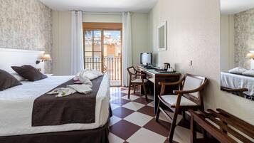 A hotel room with a bed, desk, chairs, and a balcony with a view.