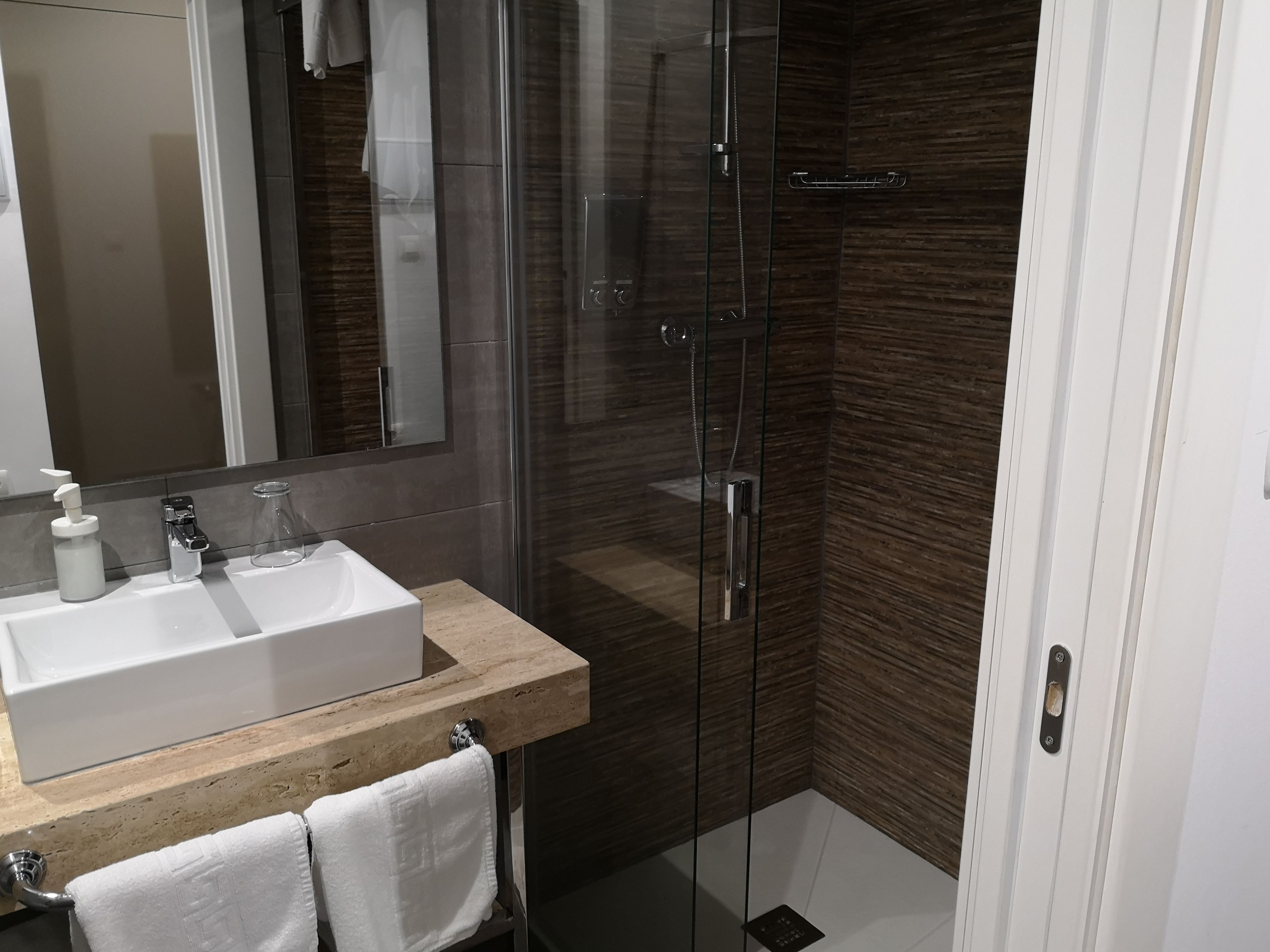 Een moderne badkamer met een douchecabine van glas, een wit wastafeltje en een spiegel.