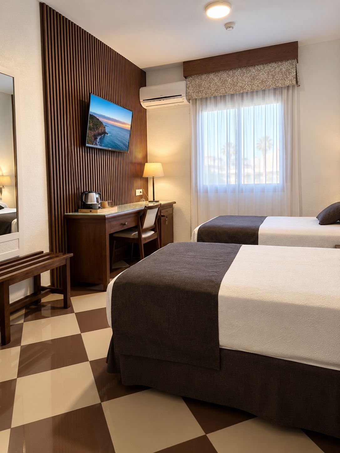 Ein Hotelzimmer mit zwei Betten, einem Schreibtisch, einem Fernseher und einem Fenster mit Vorhängen.