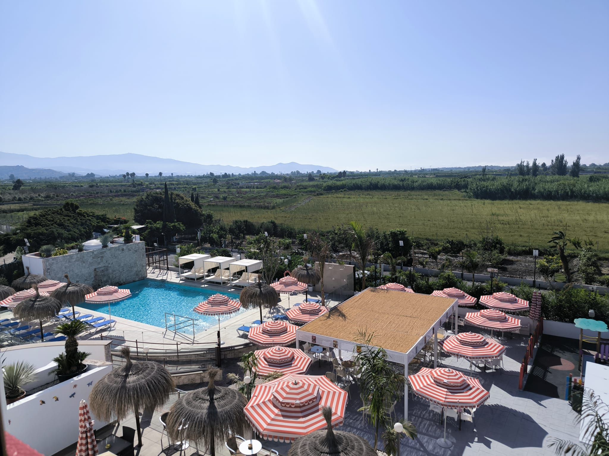 A resort with a swimming pool, outdoor seating, and a view of distant mountains.