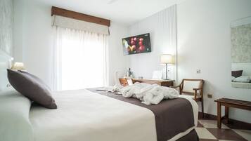 A hotel room with a large bed, a flat-screen TV mounted on the wall, a desk with a lamp, and a chair.