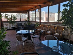 An outdoor patio with a round glass table, wicker chairs, and potted plants.