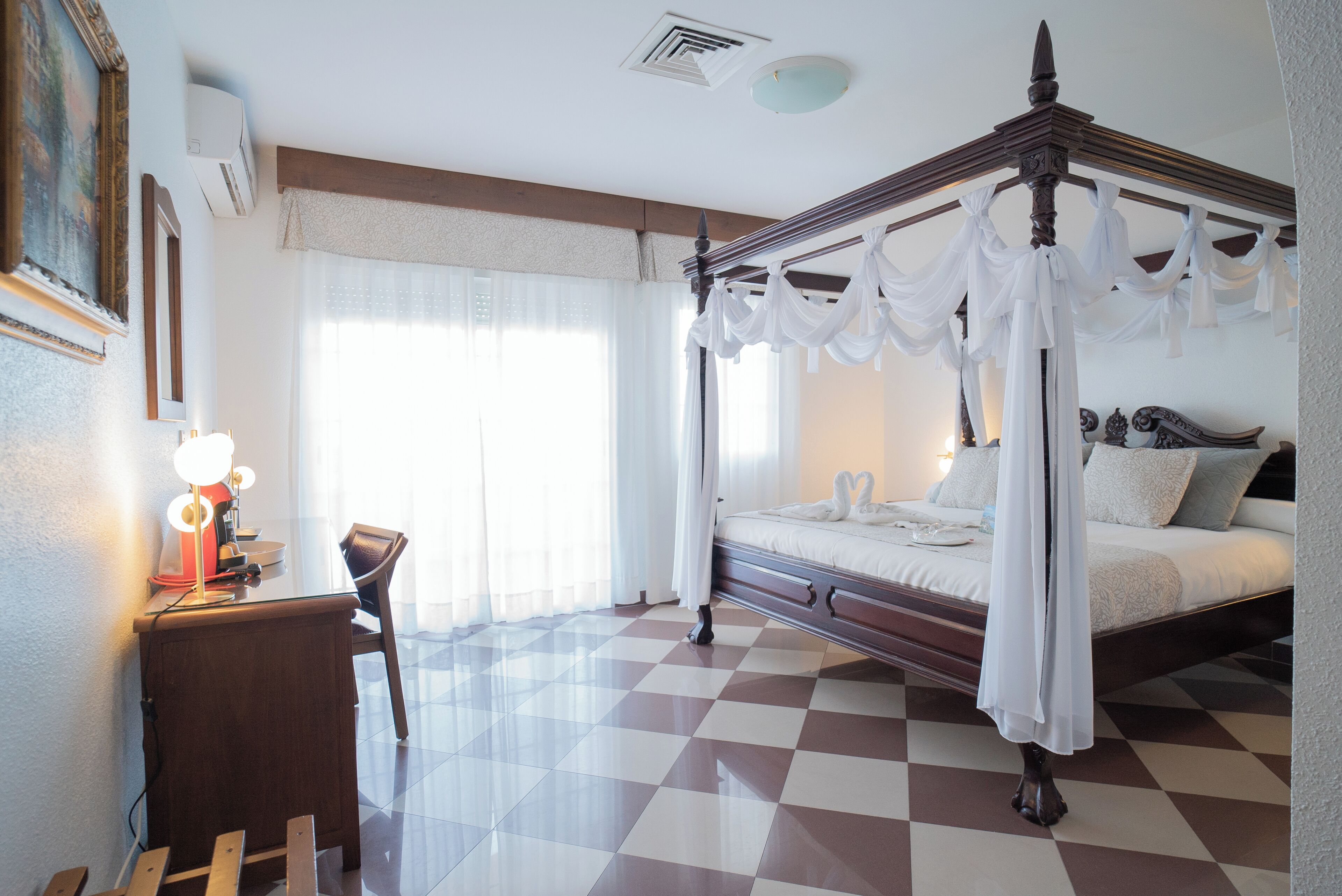 Ein Himmelbett mit weißen Vorhängen, ein Schreibtisch mit Lampe und ein Schachbrettfußboden.