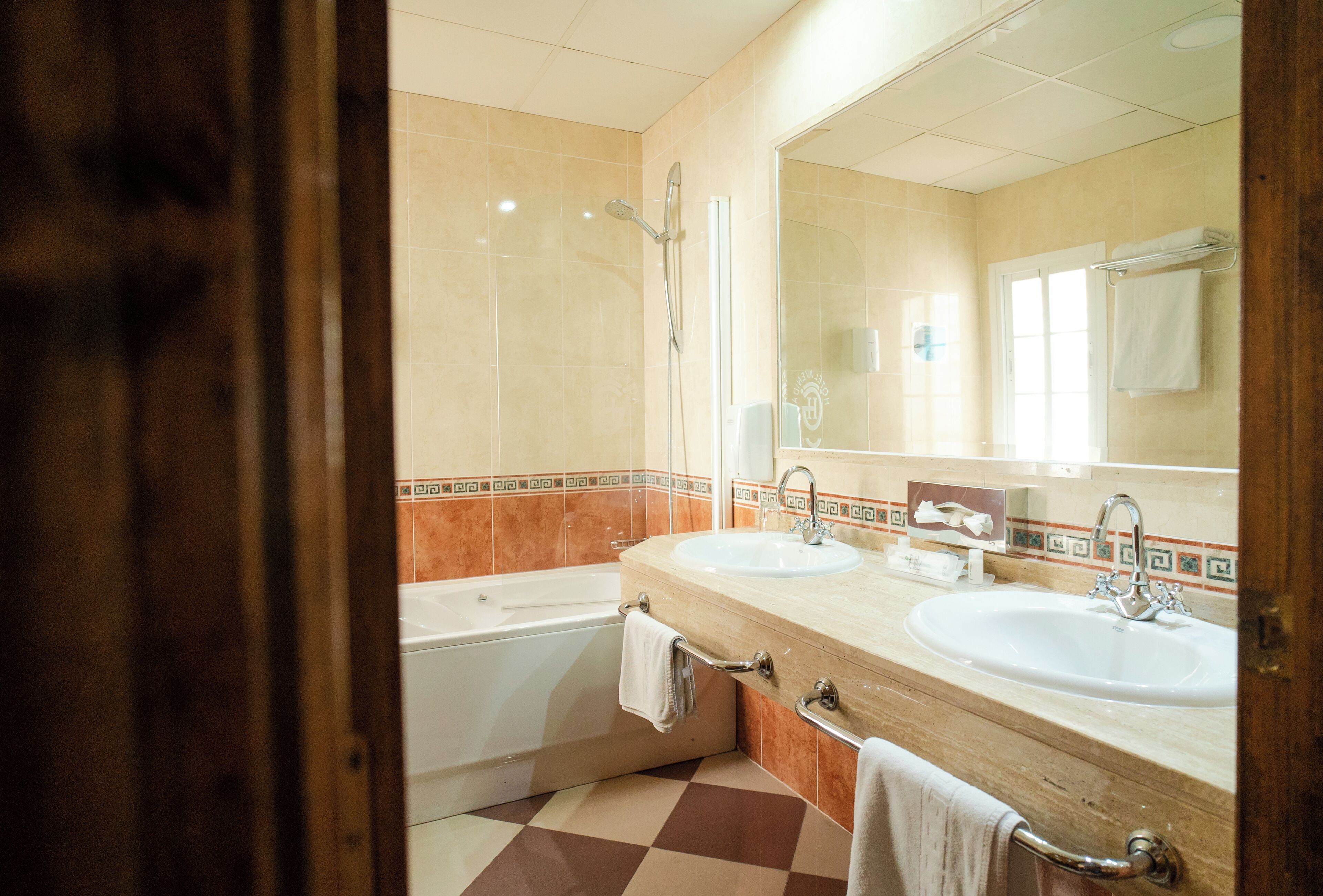 Un baño con dos lavamanos, una bañera y un espejo grande.