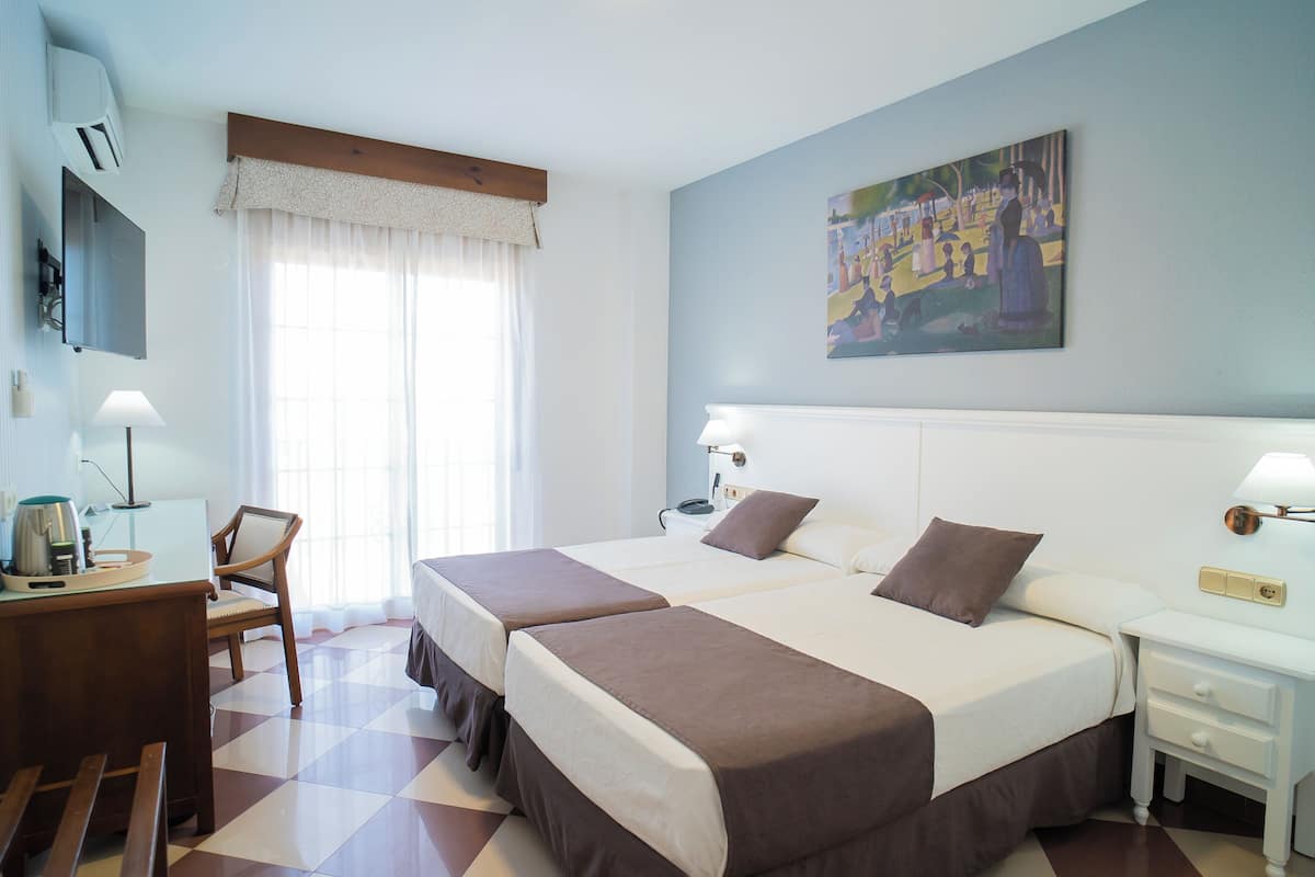 A hotel room with two beds, a desk, a chair, a TV, and a painting on the wall.
