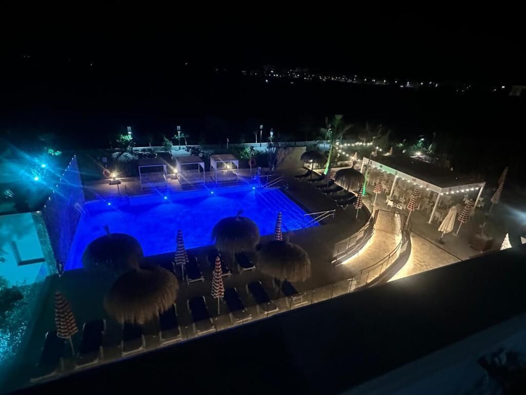 Vista nocturna de un complejo turístico con piscina, sillas de descanso y un camino bien iluminado.