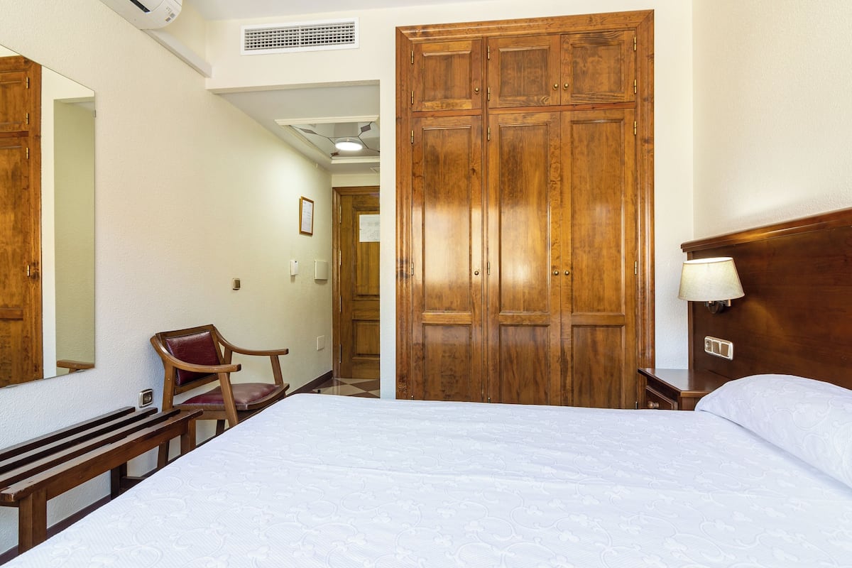 A hotel room with a large bed, a wooden wardrobe, a chair, and a bench.