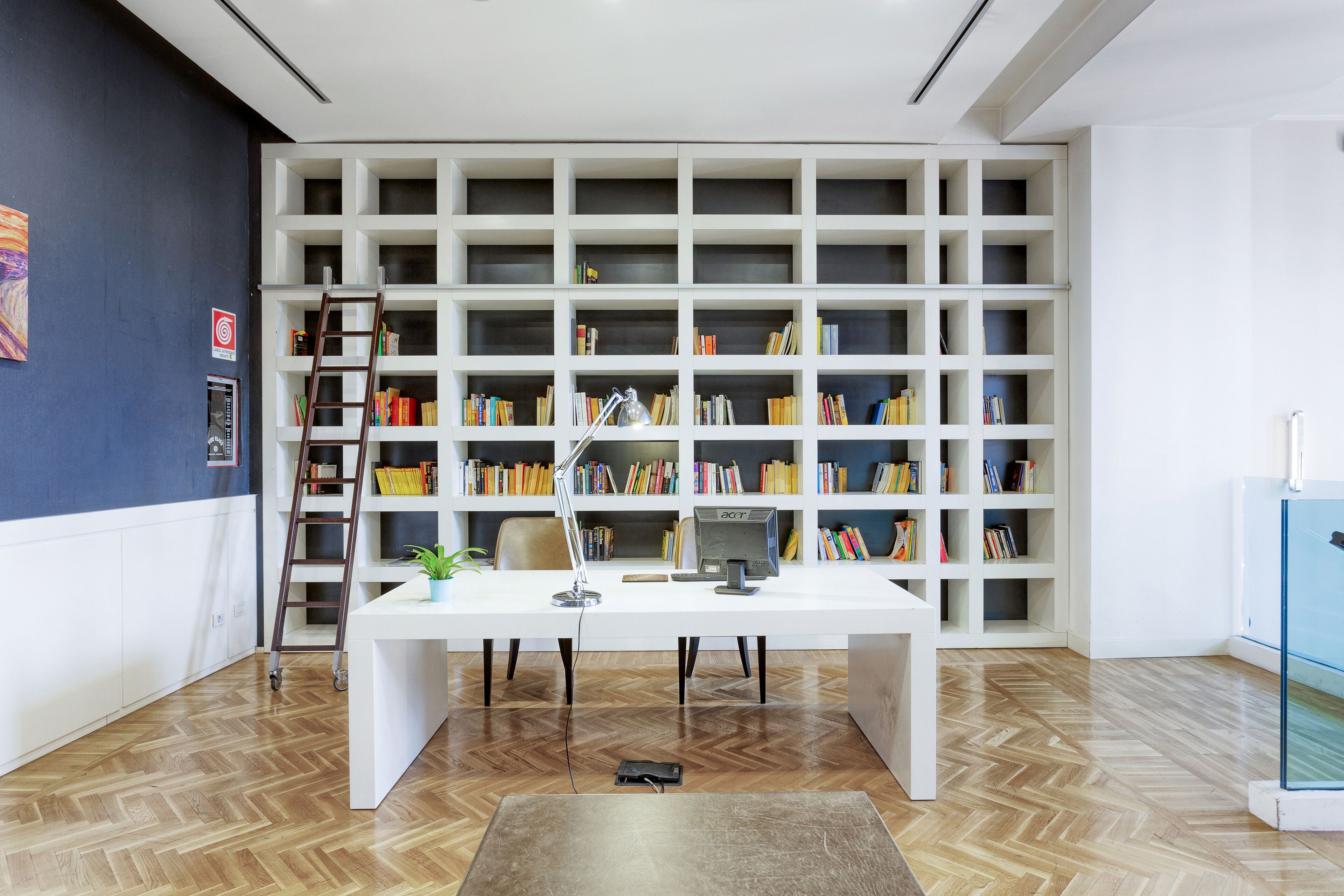 Un espacio de oficina moderno con un escritorio blanco, una computadora y estanterías llenas de libros.