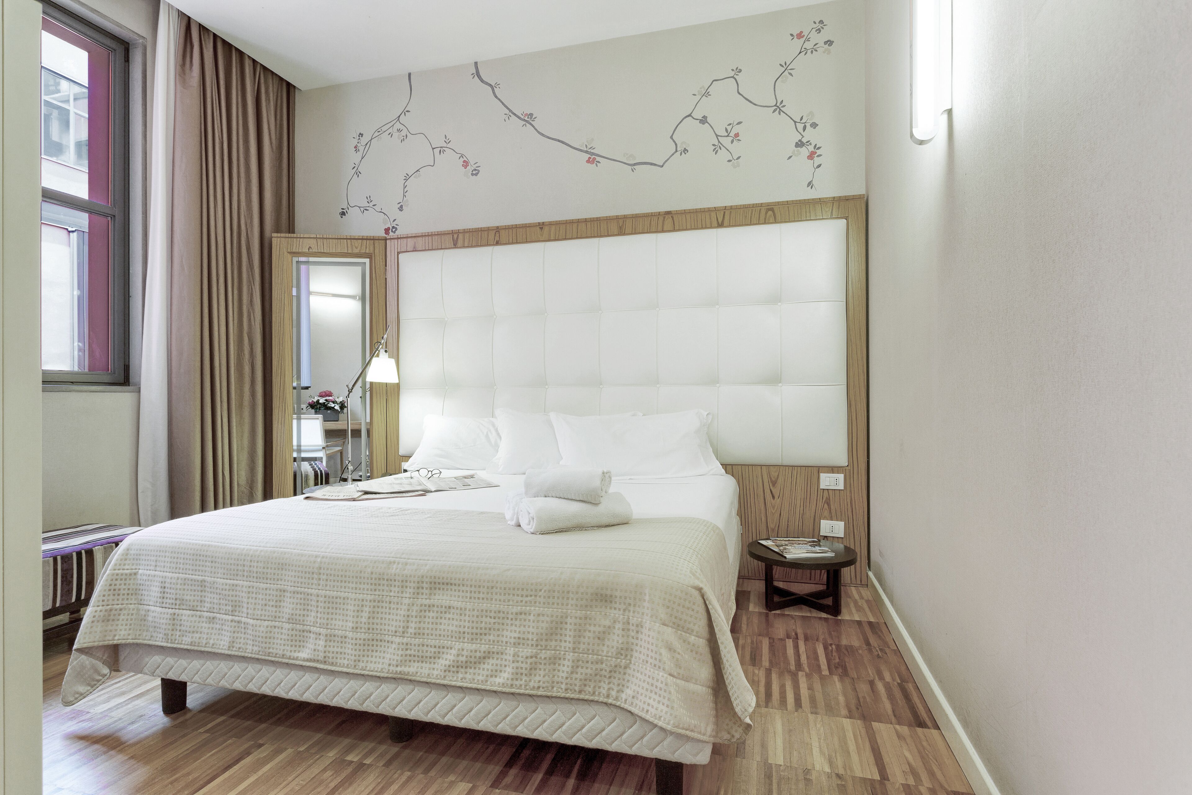 Een groot bed met een houten hoofdbord, een nachtkastje en een bedtafeltje.