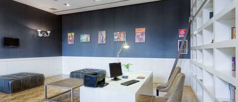 Un espacio de oficina moderno con un escritorio blanco, asientos de cuero, una estantería y obras de arte en la pared.