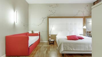 A bedroom with a bed, a red sofa, a nightstand, and a wall with a branch design.