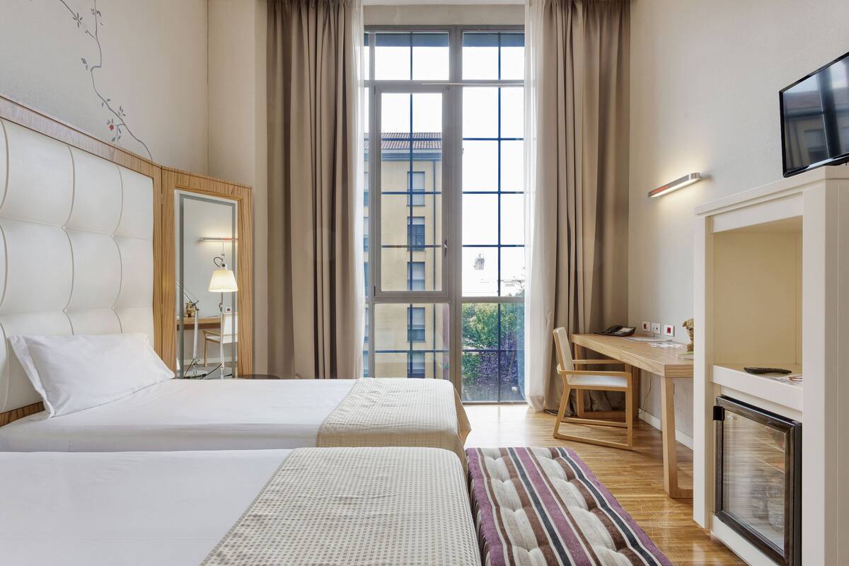 Une chambre d’hôtel avec deux lits, un bureau, une télévision et une cheminée.