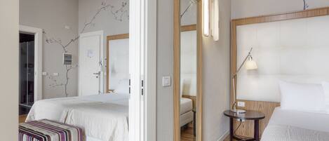 A hotel room with two beds, a bedside table with a lamp, a mirror, and a wooden floor.