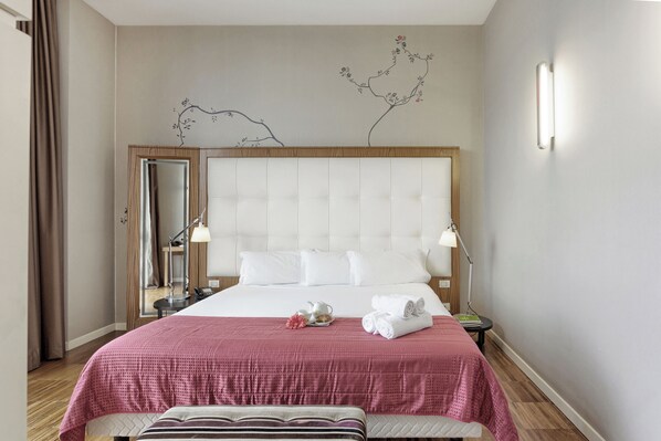 A hotel room with a large bed, a bedside table with a lamp, a mirror, and a decorative wall piece. - Italiana Hotels Milan Rho Fair (Rho)