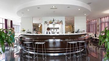 Un espace bar moderne avec un comptoir central, deux tabourets de bar et un barman.