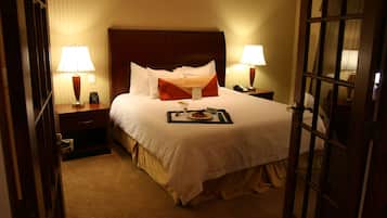 A hotel room with a large bed, two bedside tables with lamps, a nightstand, and a door.