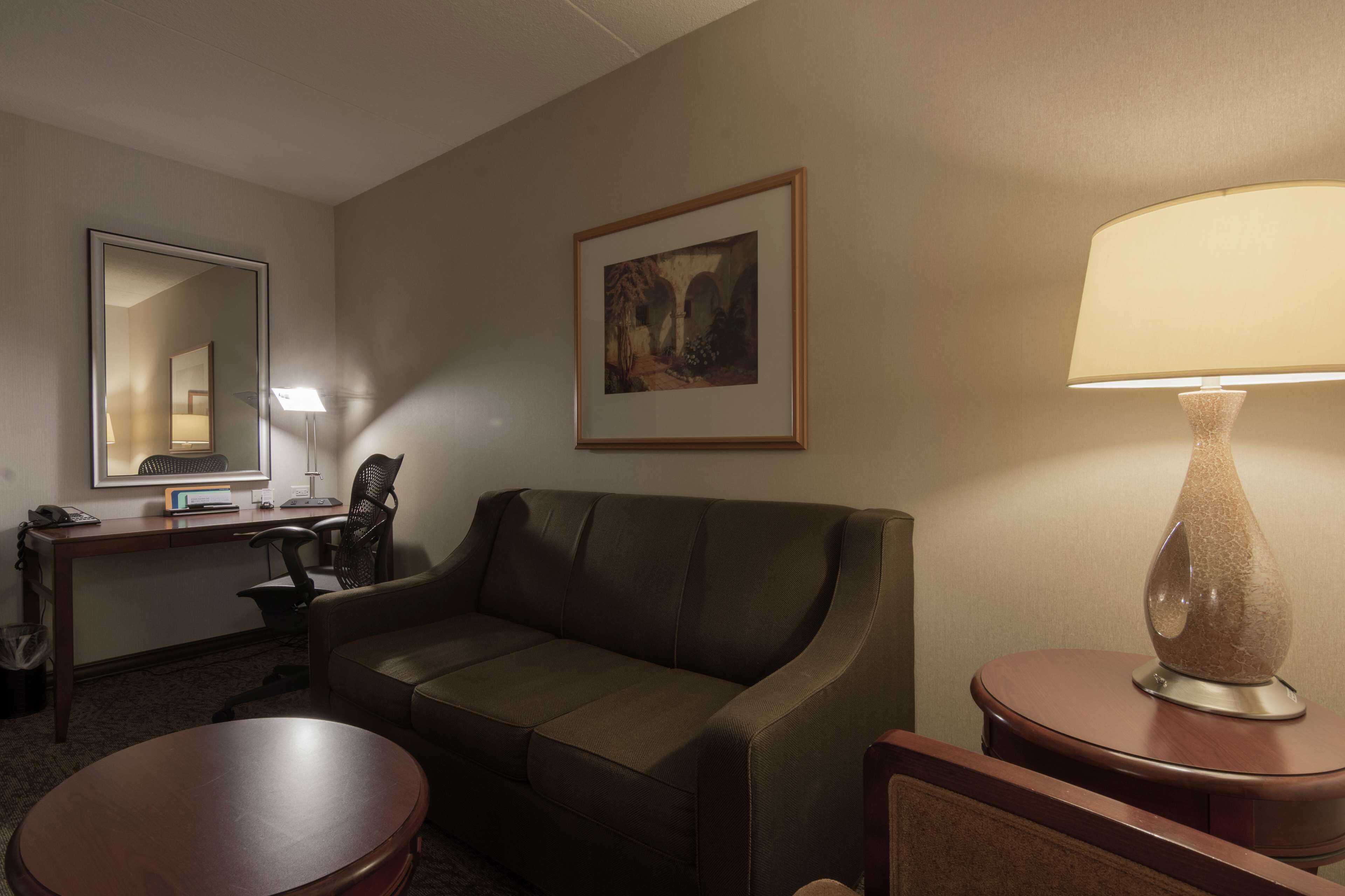Ein Hotelzimmer mit einer Couch, einem Schreibtisch mit Stuhl, einer Lampe und einem gerahmten Bild an der Wand.