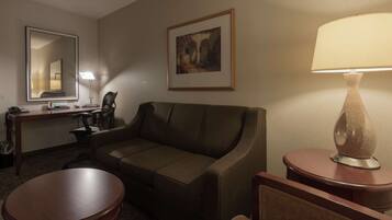 Ein Hotelzimmer mit einer Couch, einem Schreibtisch mit Stuhl, einer Lampe und einem gerahmten Bild an der Wand.