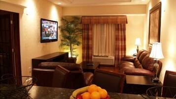 Une chambre d’hôtel équipée d’une table à manger, d’un canapé, d’une télévision et d’un panier de fruits.