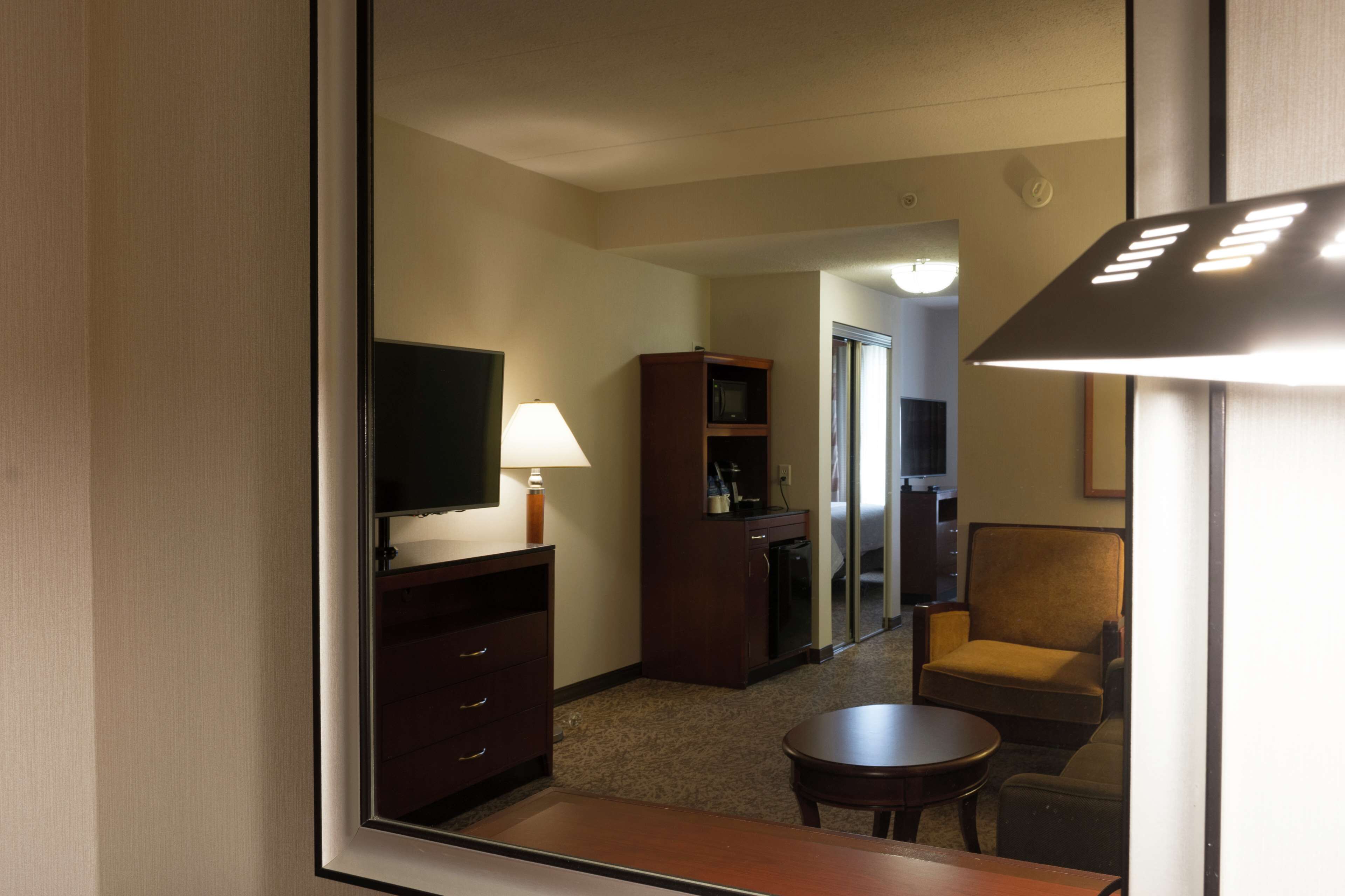 Une chambre d’hôtel équipée d’une télévision, d’un bureau, d’une chaise, d’une lampe et d’un mini-bar.