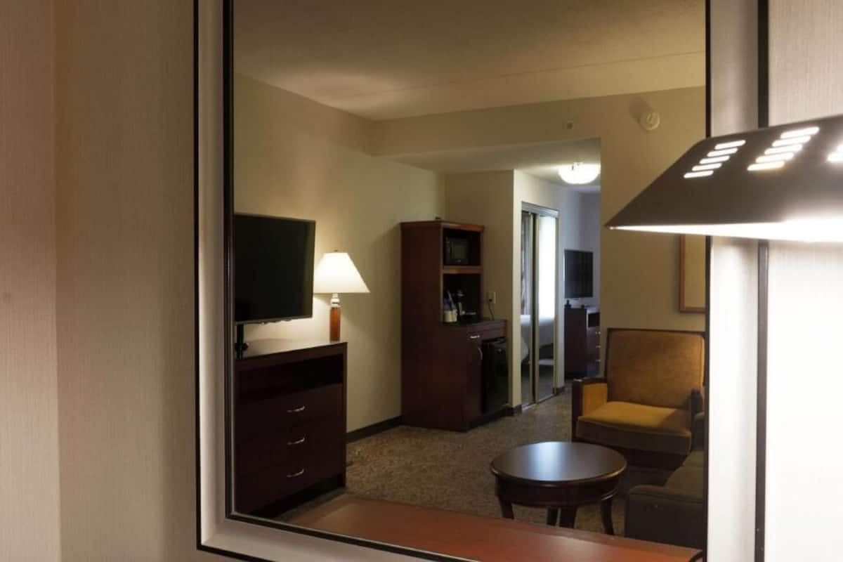 A hotel room with a television, a desk with drawers, a chair, a small table, and a lamp.