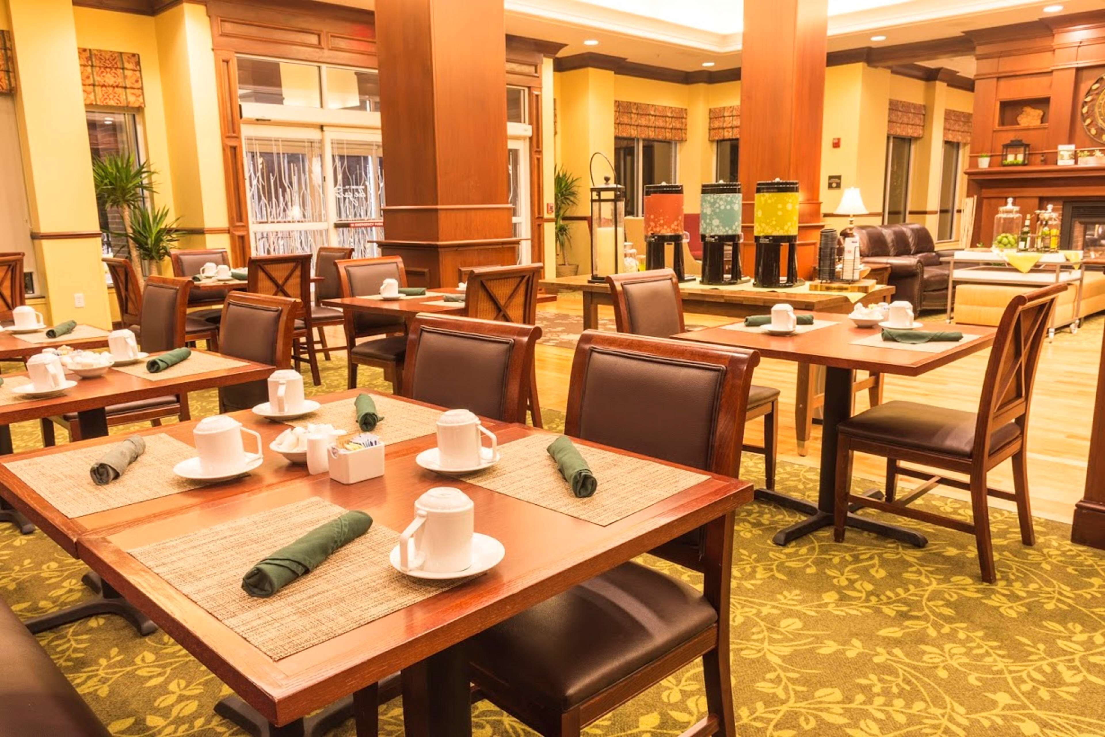 Eine Hotellobby mit mehreren Esstischen, gedeckten weißen Tellern, einem Kamin und einer Sitzecke mit Sofas und Sesseln.